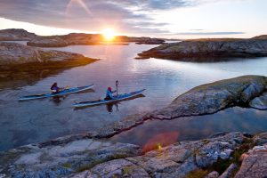 Two kayaks among small islets of stone with a sunset in the background. Photo.